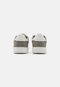 Gray suede sneakers with white leather accents, featuring a rounded back, textured sole, and a circular logo detail on the heel.
