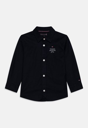 Czarna koszula z długim rękawem, zapinana na guziki, z kołnierzykiem, z logo Tommy Hilfiger oraz napisem na lewej piersi i małą flagą na lewym mankiecie.