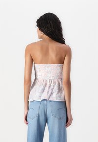 Halenka bez ramínek s květinovým vzorem v světle růžové barvě, se smockovaným živůtkem a peplum lemem. Kombinovaná s volnými modrými džíny.