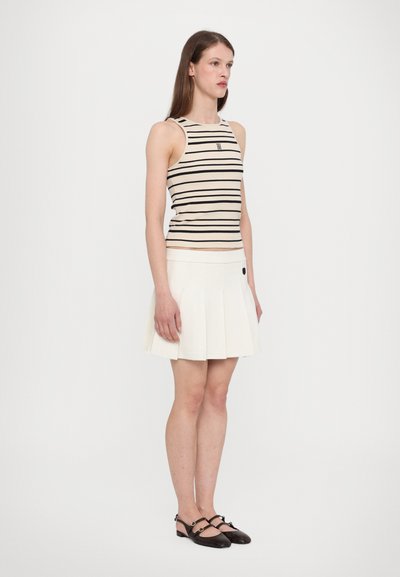 Striped beige tank top with a small logo, paired with a white pleated skirt featuring a side button. Black strap shoes complete the look.