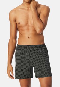 Caleçons noirs à motifs avec une ceinture élastique, présentant un design géométrique dans une teinte plus claire, fabriqués en tissu doux et respirant.