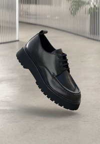 Juodas odinis batas su lygiu paviršiumi, apvaliu pirštu, raišteliais priekyje ir masyviu guminio pado, turinčio gilius raštuotus įspaudus, kad būtų užtikrinta trauka.