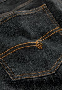 Tecido de denim negru are o buzunar posterior cu cusături galbene și un detaliu distinctiv în formă de nod. Textura pare robustă și țesută.