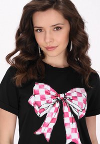 Tricou negru cu un grafic mare de fundă carouri roz, textură fină, mâneci scurte și decolteu clasic rotund.