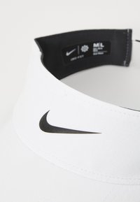 Visera blanca de Nike con un acabado texturizado, que presenta un logo negro en la parte frontal y un forro interior negro con etiquetas de tamaño y cuidado.
