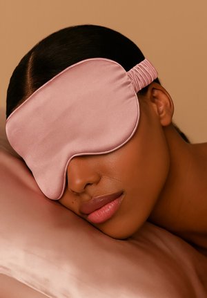 Jasnoróżowa satynowa maska na oczy do spania z elastycznym paskiem, leżąca na gładkiej, dopasowanej satynowej poduszce. Miękka tekstura i wyprofilowany kształt.