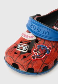 Rdeče plastične klobuke z dizajnom Spider-Mana, modrim trakom in tremi okrasnimi oznakami: "Neverjetni Spider-Man" in dvema drugima.