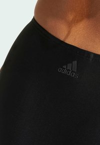 Svarta atletiska leggings gjorda av slät, elastisk tyg. Har ett sömlöst midjeband och en texturerad logotypaccent vid höften.
