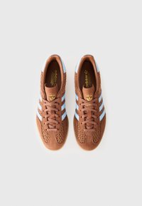 Par tenisica u smešnoj boji marke Adidas s svetloplavim trakama, teksturiranim tkanim stranama i bež đonovima, prikazanih odozgo na beloj pozadini.