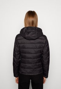 Veste matelassée noire avec motif matelassé horizontal, capuche attachée et manches longues. Matériau lisse et brillant avec une silhouette ajustée.