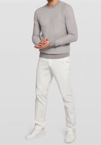 Jersey de punto gris claro con cuello redondo, puños y bajo acanalados. Combinado con chinos blancos y zapatillas blancas, manos juntas.