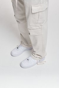 Pantaloni cargo beige con molte tasche e sneakers bianche con dettagli perforati e lacci. Design semplice e funzionale con un aspetto pulito.