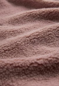 Mjukt rosa fleece tyg med en texturerad yta, som visar veck och rynkor, vilket framhäver dess plyschiga och mysiga kvalitet.