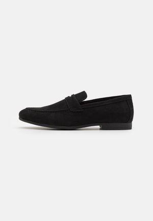 Mocassins en daim noir avec un bout arrondi, un design sans lacets et une semelle en caoutchouc basse. Présente un accent cousu le long de la partie supérieure.
