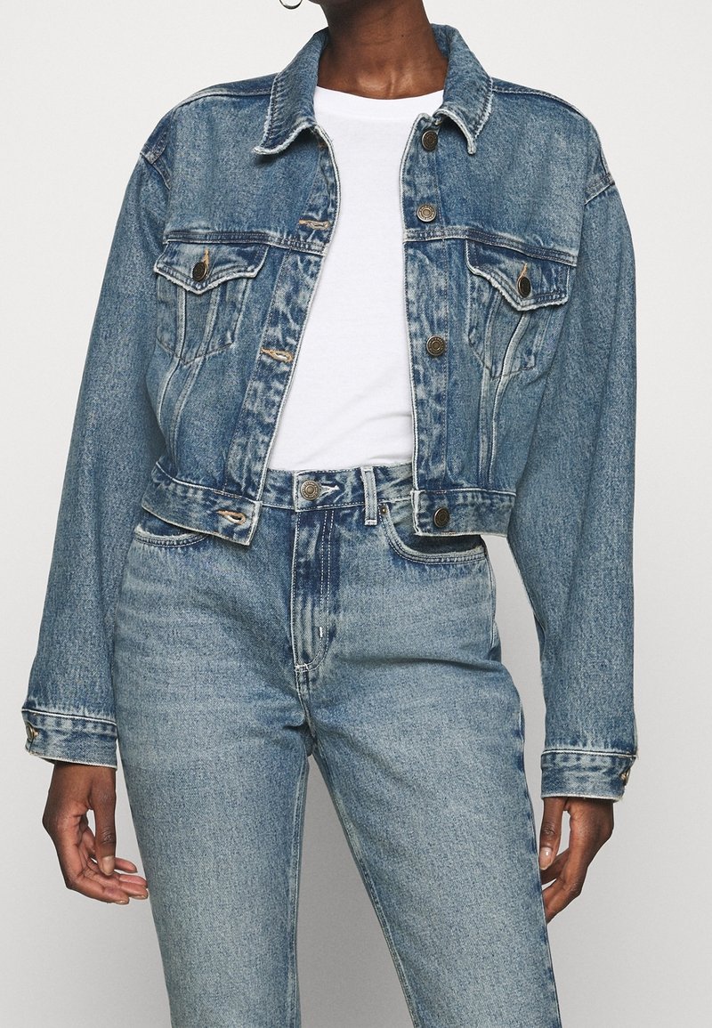 Blå denimjacka med cropped design, knappstängning framtill, två bröstfickor och traditionell krage. Kombinerad med högmidjade blå jeans.