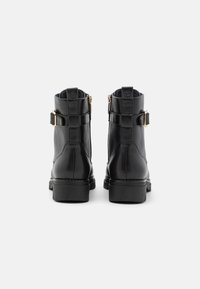Bottines noires en cuir avec une finition lisse, fermetures éclair sur le côté et accents de boucle décorative. Semelles robustes et texturées offrant une bonne adhérence.