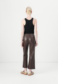 Brune faux skinnbukser med høy midje og vide ben, kombinert med en svart tanktopp og beige joggesko med teksturert såle.