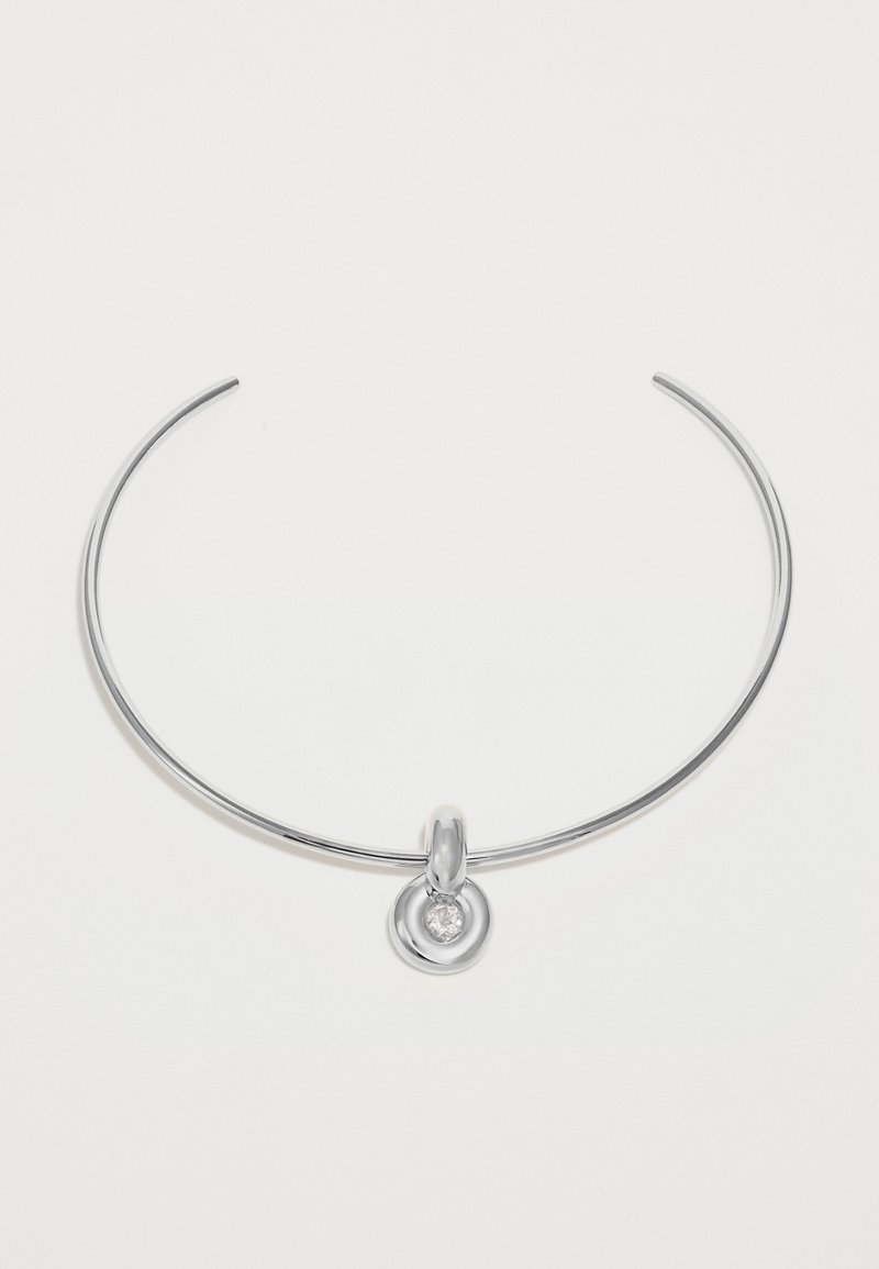 Tenká strieborná náhrdelník s kruhovým príveskom, v ktorom sa nachádza malý číry drahokam v strede, na bielom pozadí.