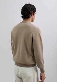 Beige gebreide trui met lange mouwen, ronde hals en geribbelde manchetten, gecombineerd met lichtgekleurde broek. Soepele textuur, casual pasvorm.