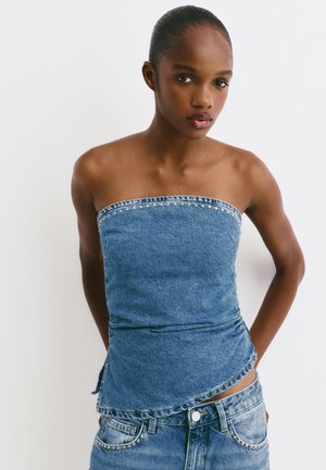 Top senza spalline in denim con una silhouette aderente, orlo sfrangiato e dettagli con borchie lungo il colletto, abbinato a jeans coordinati.