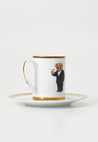 Bijela porcelanska šalica i tanjurić sa zlatnim obrubom, na kojem se nalazi medvjedić u smokingu koji drži čašu martini.