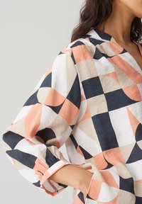 Camicia larga in cotone con un motivo geometrico. Presenta colori in pesca, blu navy, bianco e beige, con maniche arricciate.