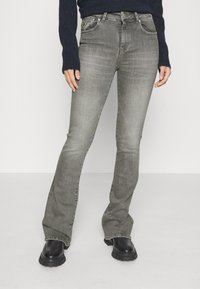 Jeans a zampa grigia realizzati in denim, con un classico design a cinque tasche e chiusura con bottone metallico, abbinati a stivali neri con suola spessa.