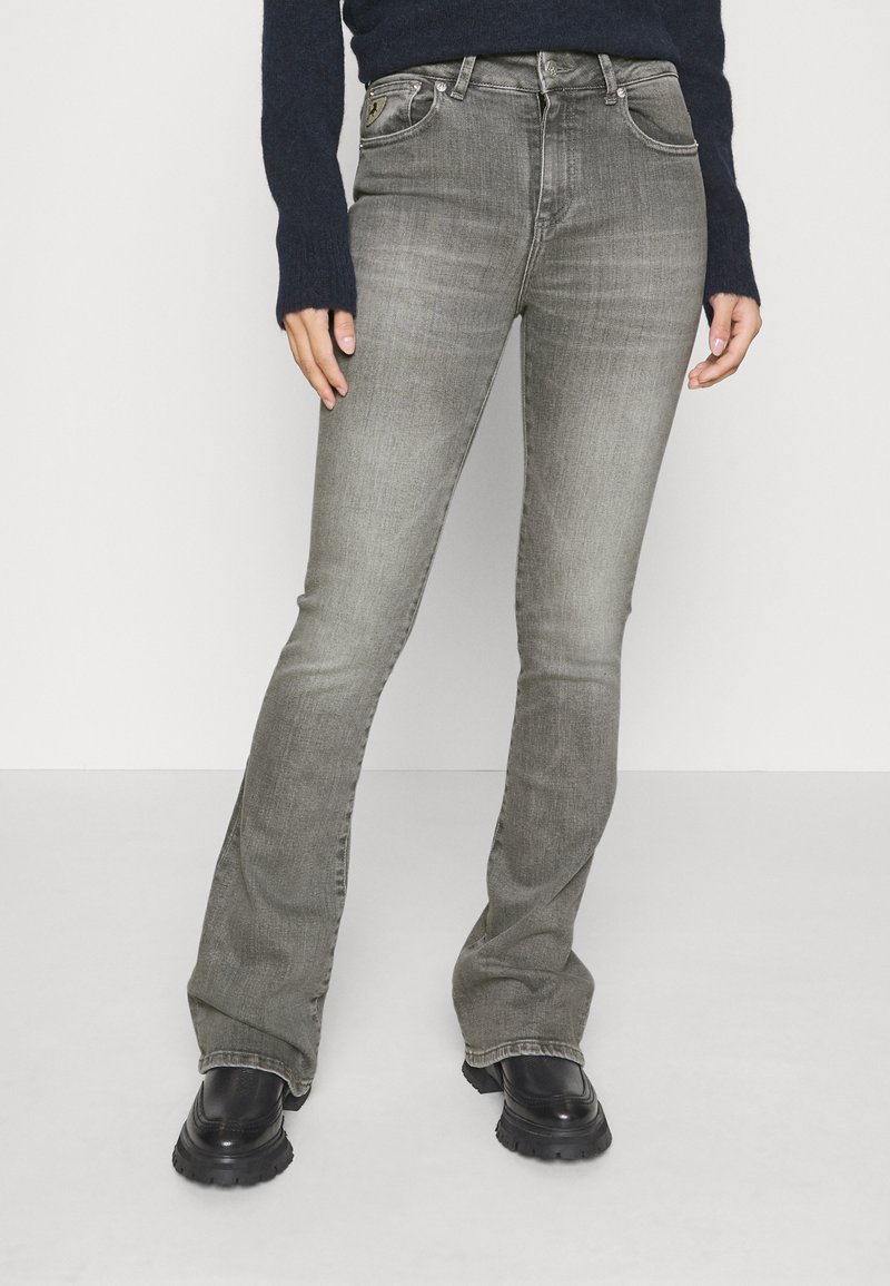Jeans a zampa grigia realizzati in denim, con un classico design a cinque tasche e chiusura con bottone metallico, abbinati a stivali neri con suola spessa.