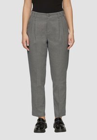 Graue Hose mit maßgeschneidertem Schnitt, mit Bundfalten, Gürtelschlaufen, Knopfverschluss und schmal zulaufendem Saum. Getragen mit schwarzen Slippern.