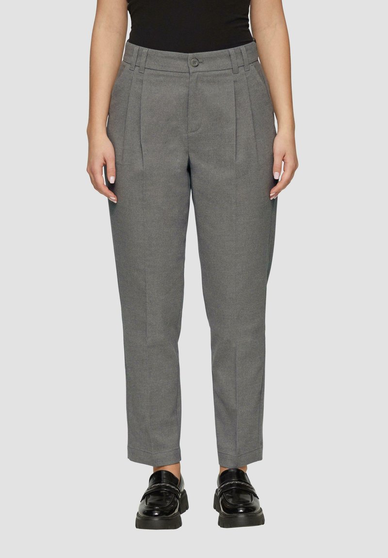 Graue Hose mit maßgeschneidertem Schnitt, mit Bundfalten, Gürtelschlaufen, Knopfverschluss und schmal zulaufendem Saum. Getragen mit schwarzen Slippern.