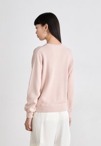 Sweatshirt rosa claro com um corte descontraído, gola e punhos canelados, e uma textura suave. Apresenta ombros caídos e uma bainha encaracolada à altura da cintura.