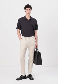 Crna polo majica, bež platneni hlače s vezicom, crne kožne cipele, drži crnu torbu. Jednostavan, krojen silueta.