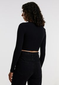 Schwarzes, tailliertes Langarm-Rippoberteil mit passender Silhouette, kombiniert mit hochgeschnittenen schwarzen Jeans aus Denim mit Gesäßtaschen.