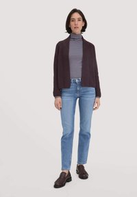 Dunkelviolette offene Strickjacke über einem gestreiften Rollkragenpullover, kombiniert mit hellblauen Jeans und braunen Mokassins mit Fransen. Texturierte Stoffdetails sind sichtbar.