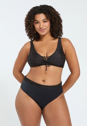 Kvinde med krøllet hår iført en sort zebra-print bikini top med snøring foran og matchende høj taljede bikini underdele, smilende.