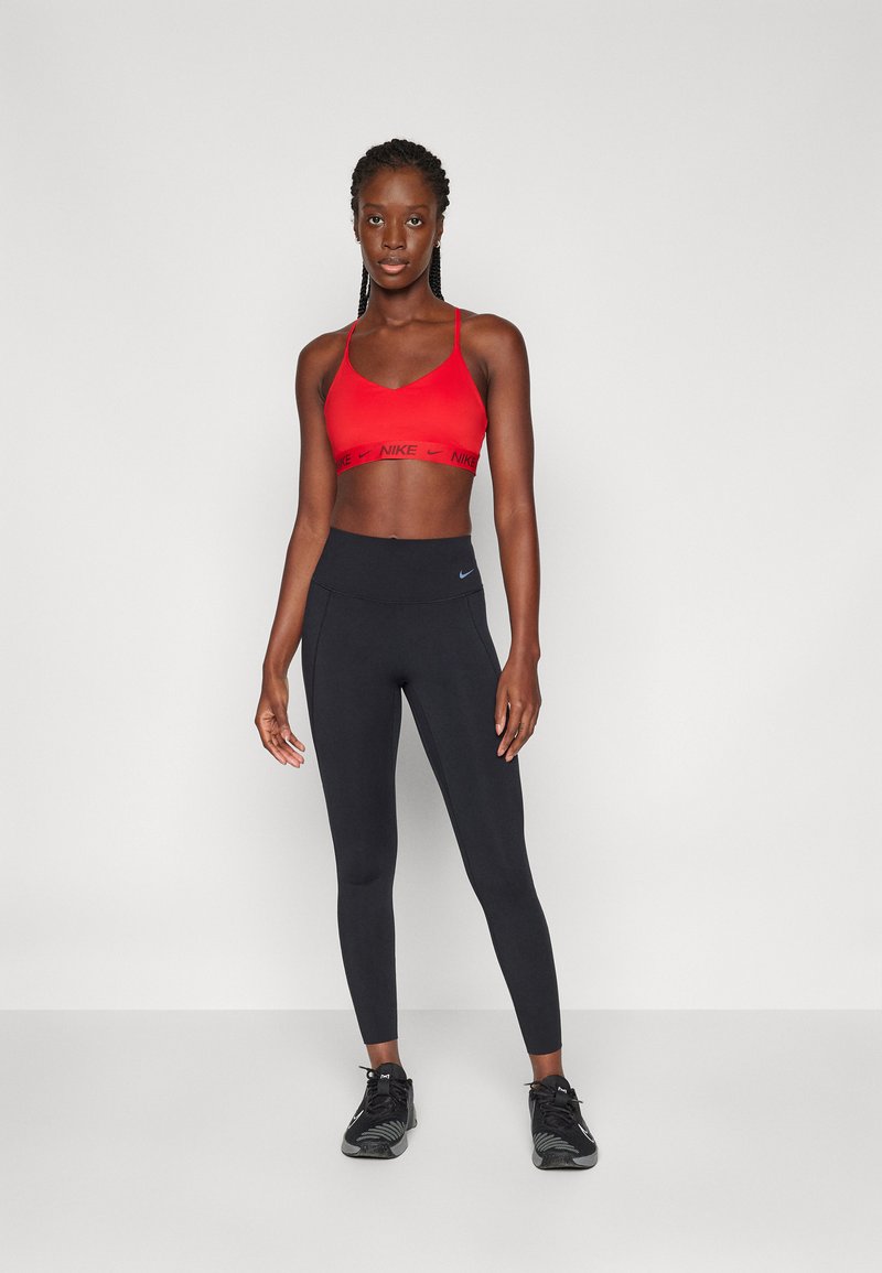 Rode sportbh met zwarte Nike-branding, gecombineerd met hoge zwarte leggings en zwarte sportschoenen, op een neutrale achtergrond.