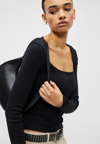 Juoda palaidinė ilgomis rankovėmis, kvadrato formos iškirpte ir dekoratyvine siūle. Derinama su juoda rankine ir smėlio spalvos kelnėmis su kniedėtu diržu.