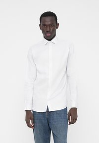 Weißes Hemd mit langen Ärmeln und Kragen, das eine dezente Textur aufweist. Kombiniert mit blauen Jeansstoffen.