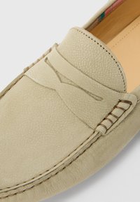 Mocassin en cuir beige clair avec des coutures détaillées et un design classique à bride à penny sur le dessus.