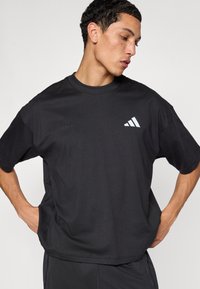 Černé bavlněné sportovní tričko s krátkými rukávy, zdobené vyraženým nápisem „adidas running“ a bílým logem s třemi pruhy na hrudi.