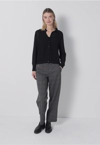 Zwarte button-up blouse met lange mouwen, gecombineerd met grijs geruite wijde broek en zwarte enkelboots. Eenvoudig ontwerp, zachte textuur.