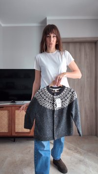 Szürke kötött kardigán mintás krémszínű vállrésszel, gombos előlappal és hosszú ujjakkal, fa vállfára akasztva. Címke látható.