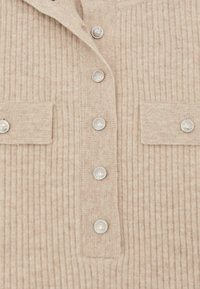 Bordázott bézs kötött kardigán ezüst gombokkal, két mellzsebbel és klasszikus gallér dizájnnal. Puha tapintású, enyhén fényes felülettel.