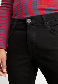 Melnas denima bikses ar cieši pieguļošu dizainu, kuru īpašības ir pogu aizdare, diskrēta šuvju apdare un gluda tekstūra.