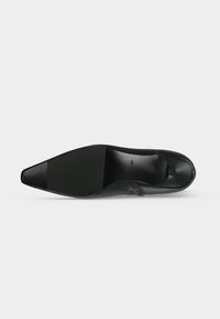 Semelle de chaussure habillée noire à bout pointu avec un petit talon et une surface texturée au niveau de la plante du pied et du talon.