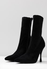 Svarta mocka ankle boots med spetsiga tår, höga stilettklackar och siddragkedjor. Slät textur med en figuranpassad design.