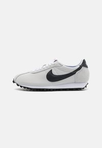 Sivi tenisice s crnim akcentima, teksturiranom gornjom površinom, bijelim vezicama i bijelim međuslojem. Imaju crni Swoosh logo i teksturiran potplat.