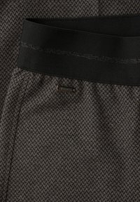 Gestructureerde donkergrijze stof met visgraatmotief, voorzien van een zwarte elastische tailleband en een metalen merkembleem vlakbij de taille.