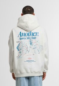 Sudadera gris claro con capucha, que presenta un gráfico colorido de un mapa de esquí en la parte posterior, con el texto "Otro Club Après Ski" destacado.