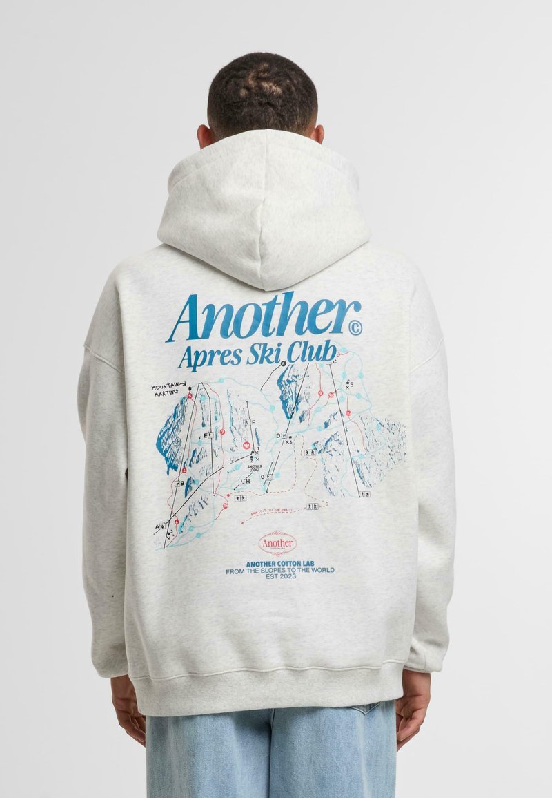 Sudadera gris claro con capucha, que presenta un gráfico colorido de un mapa de esquí en la parte posterior, con el texto "Otro Club Après Ski" destacado.